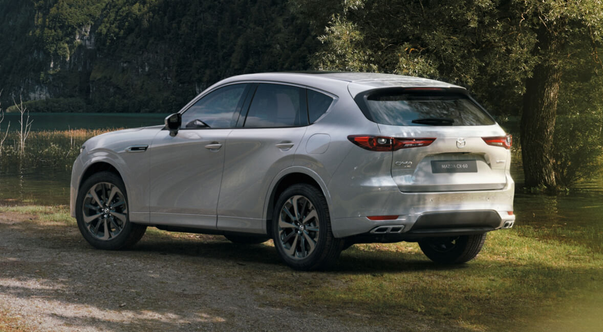 The all-new Mazda CX-60 Plug-In Hybrid SUV shown from the rear parked outside in a tree-filled meadow.  