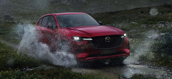 The all-new Mazda CX-60 Plug-In Hybrid SUV splashing through a puddle on a mountain road